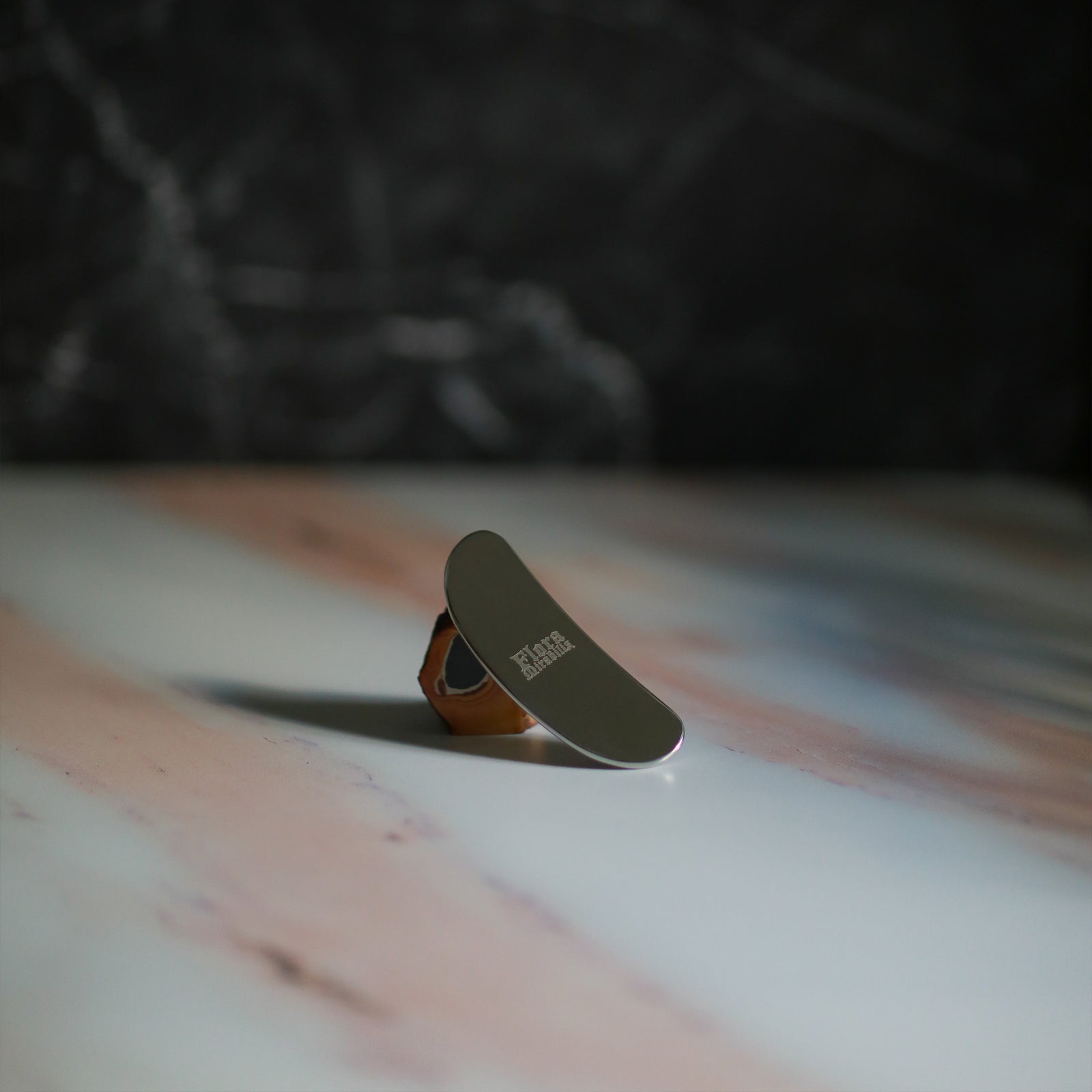 Flora Mirabilis Stainless Steel Beauty Tool on marble table with dark background.