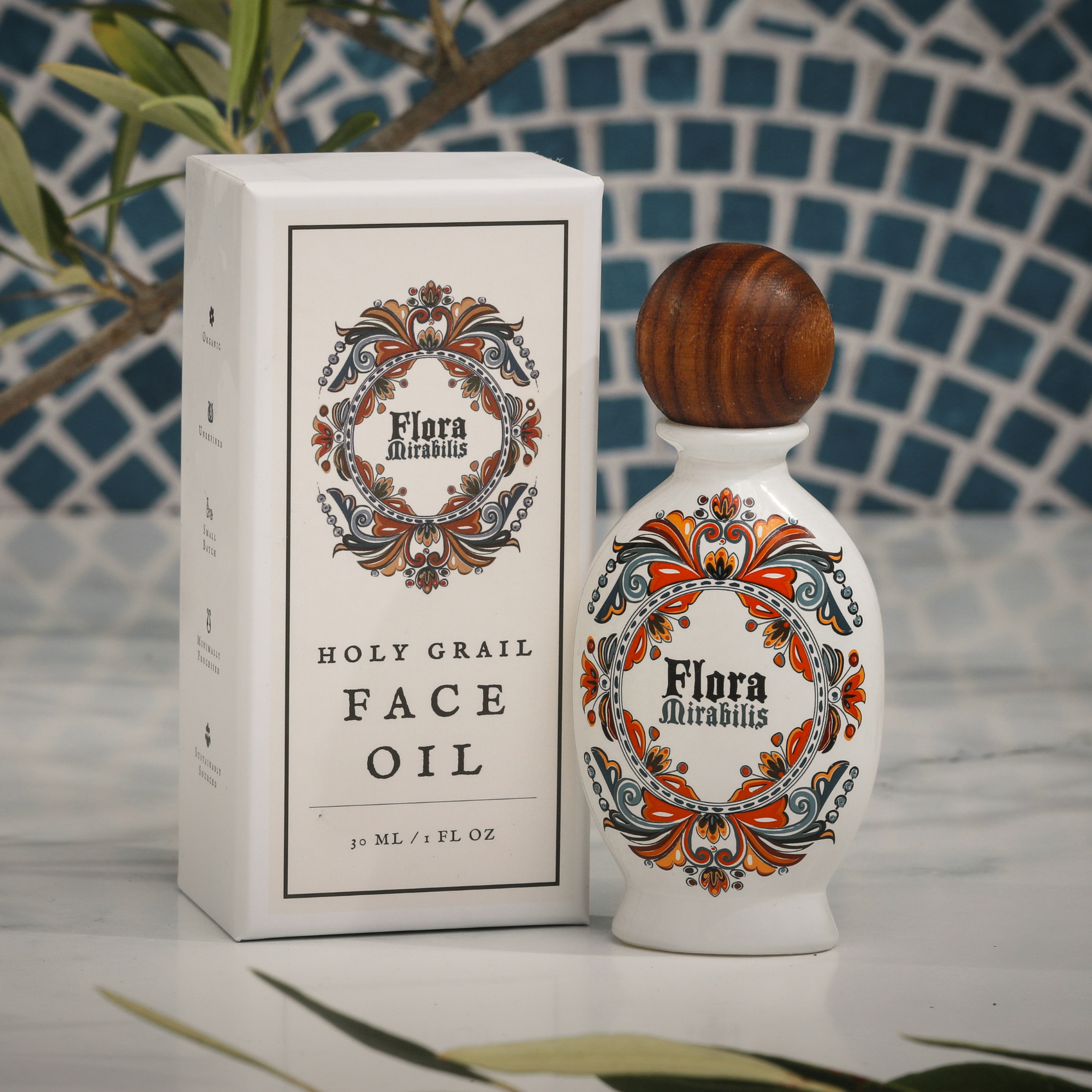 Flora Mirabilis Holy Grail Face Oil bottle and packaging displayed on marble surface with mosaic tile background.
