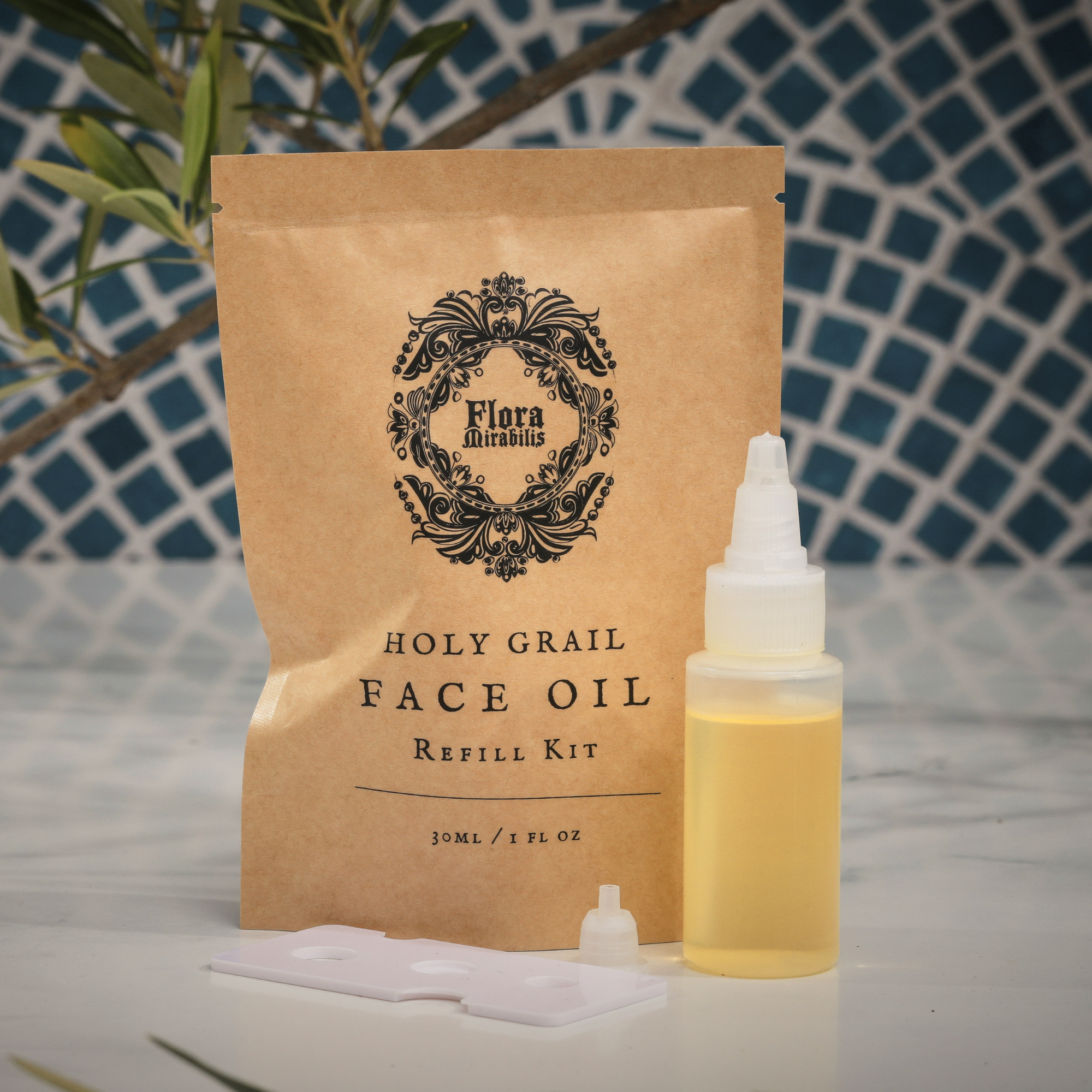 Flora Mirabilis Holy Grail Face Oil Refill Kit with kraft pouch, refill bottle, and dispensing accessories displayed on a marble surface.