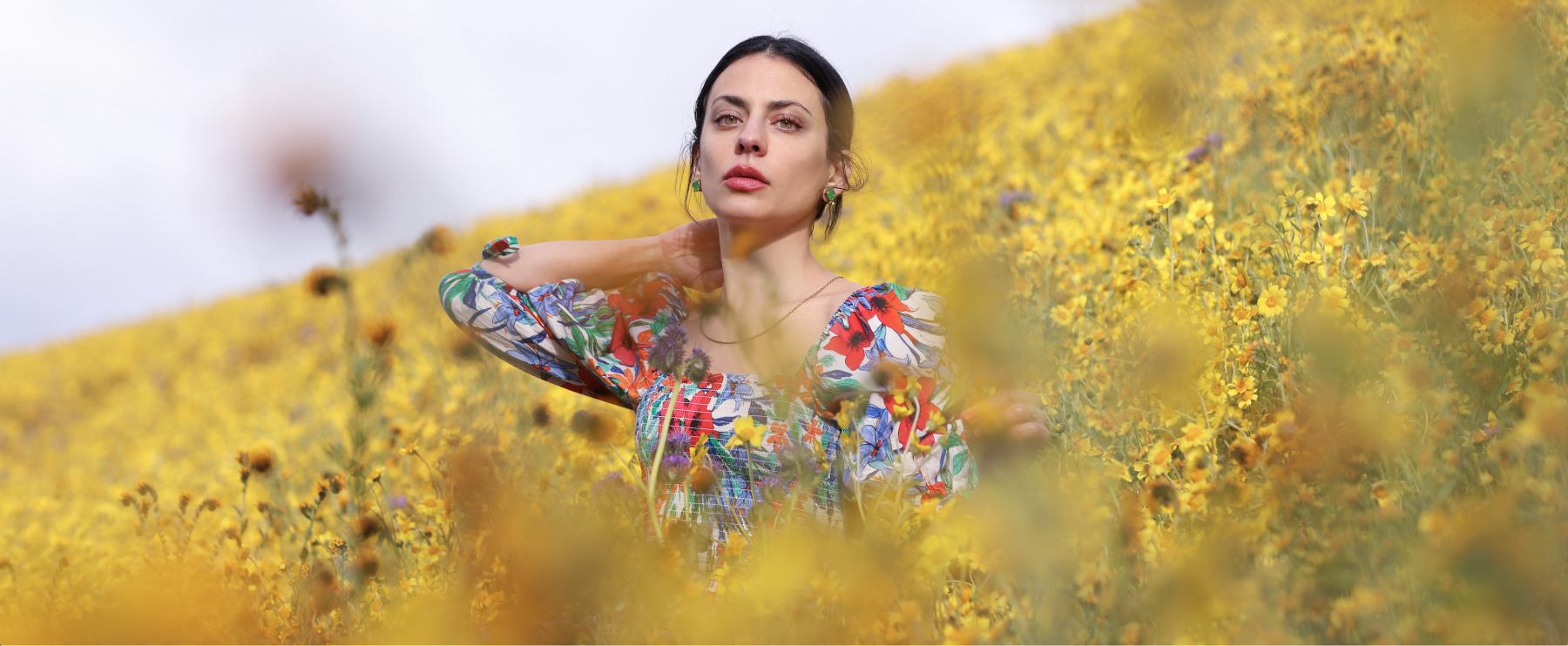 Jordan LaFragola in a colorful dress standing amidst yellow flowers looking at nature for inspiration for natural skincare ingredients